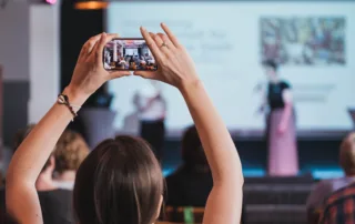 Eine Frau von hinten die ein Handy in die Luft hält und eine Bühne fotografiert