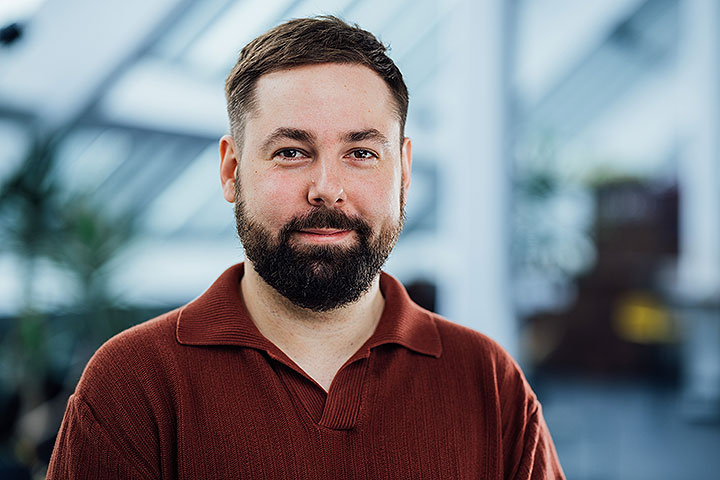 Daniel Mittelstädt, Jüngerer Mann mit braunem Haar und braunem Bart, er trägt ein dunkelrotes Shirt mit Kragen und lächelt
