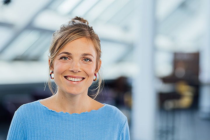 Weiße blonde Frau mit hochgebundenem Haar und hellblauem Shirt lächelt freundlich