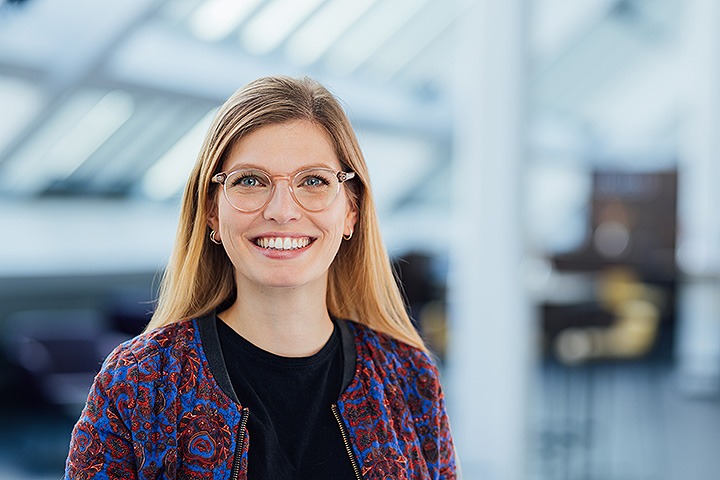 Weiße blonde Frau mit Brille und geblümter Jacke lächelt freundlich