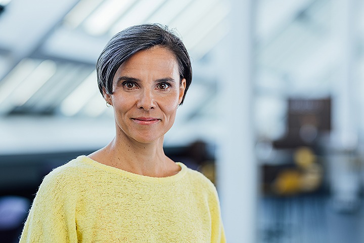 Weiße Frau mit kurzem dunkelgrauem Bob und hellgelbem Shirt lächelt in die Kamera