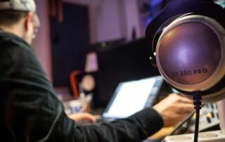 Ein rundes Mikro im Vordergrund, dahinter ein Mann am Laptop mit Kopfhörern, den man nur von hinten sieht